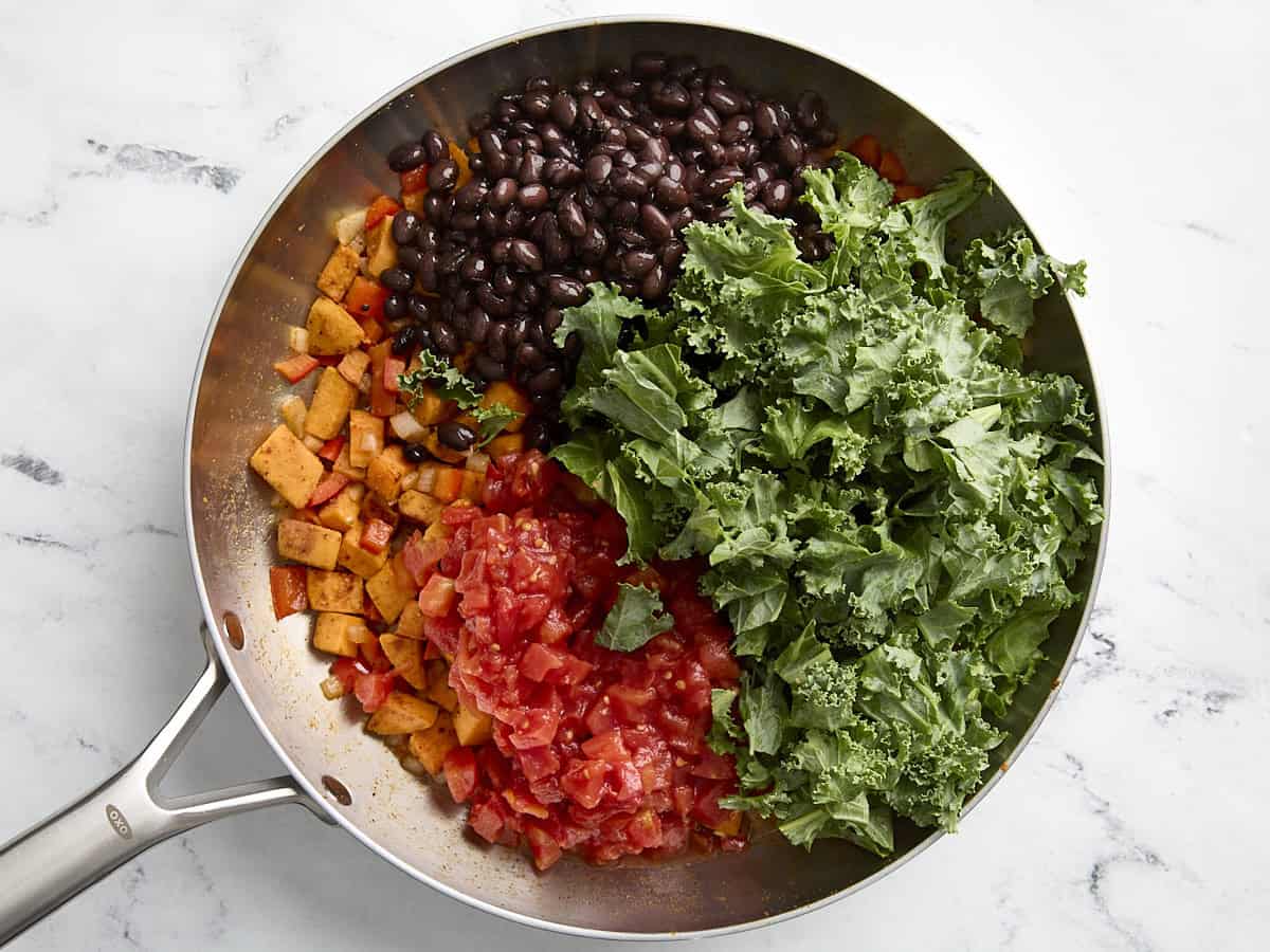 Kale, black beans, and tomatoes added to sweet potatoes in a skillet.