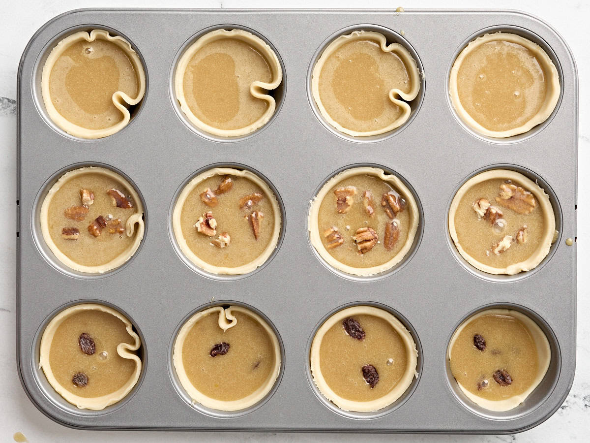 Pie crusts in a cupcake tin filled with butter tart filling.