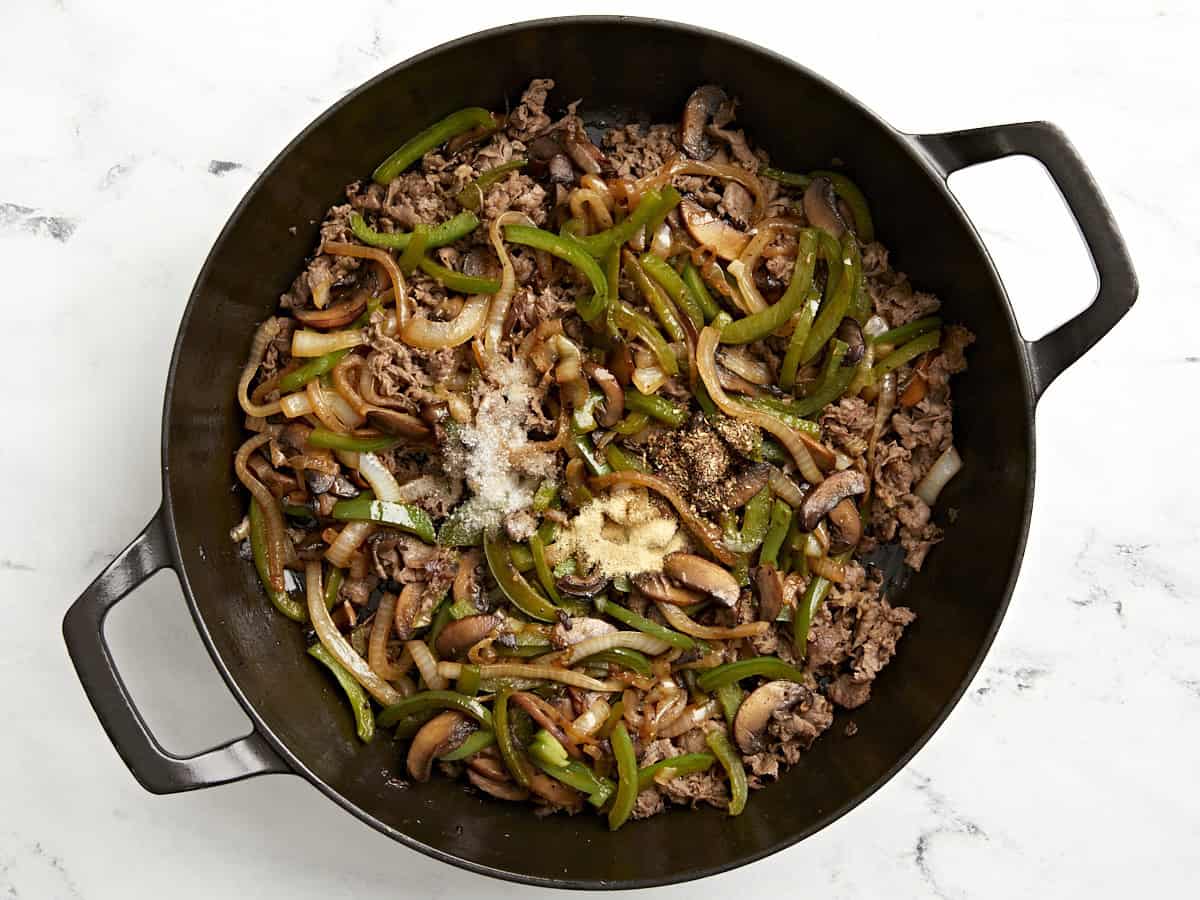 Peppers and onions added to cooked beef in the skillet.