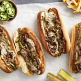 Overhead view of philly cheesesteak sandwiches on parchment paper with fries on the side.