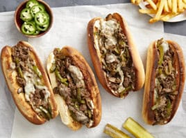 Overhead view of philly cheesesteak sandwiches on parchment paper with fries on the side.