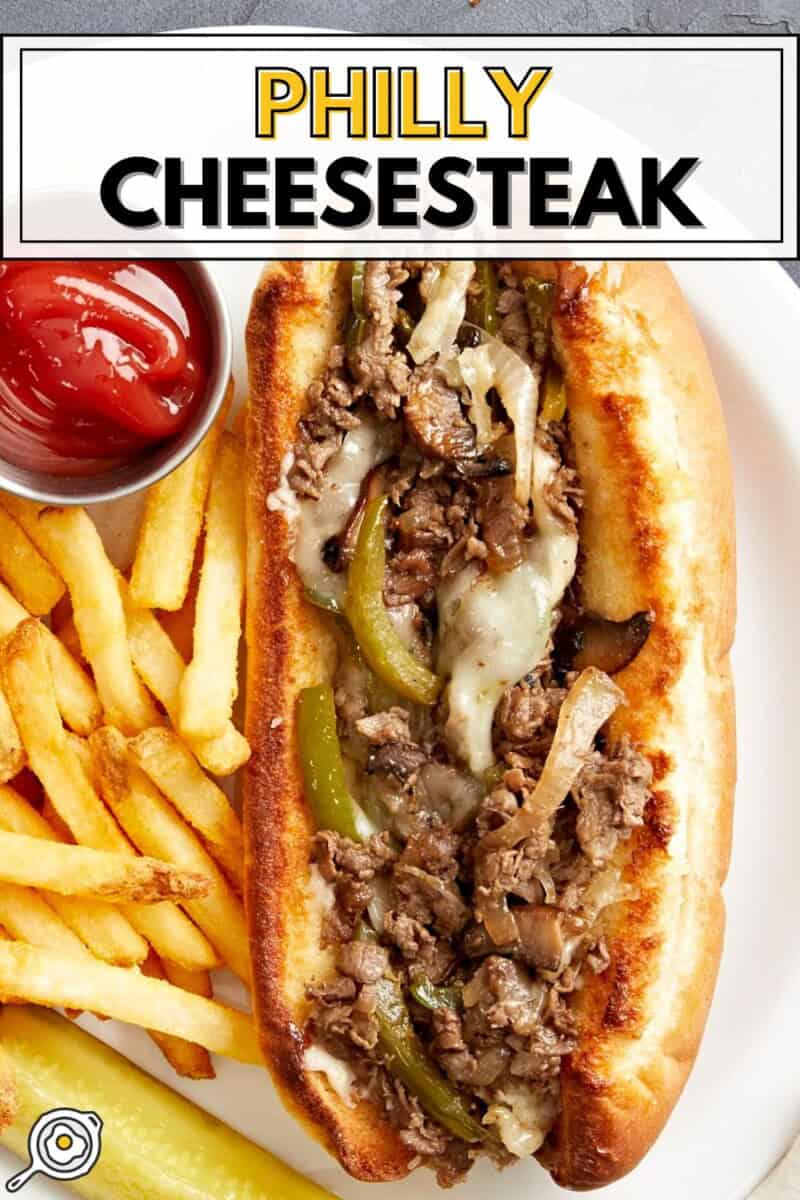 Overhead view of a philly cheesesteak with fries on the side on a white plate.