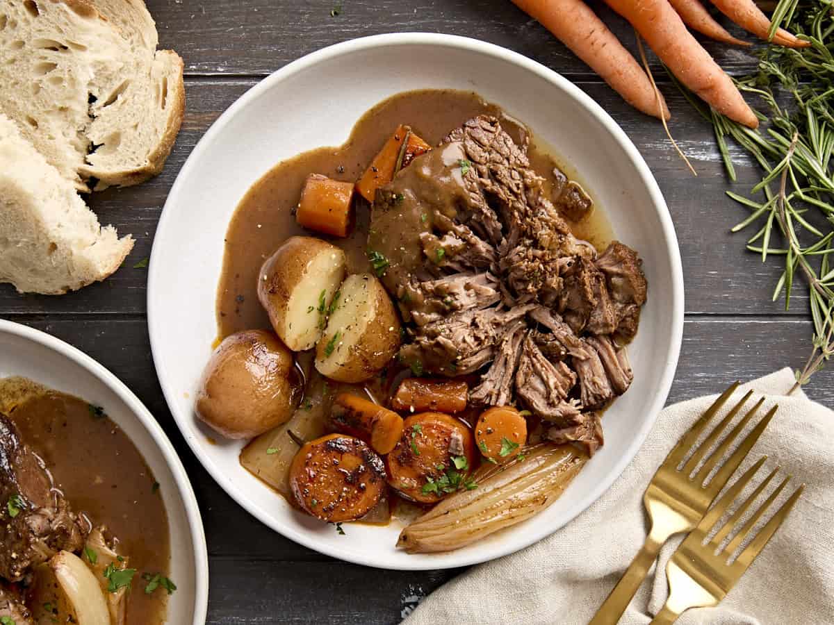 A pot roast and vegetables on a white plate.