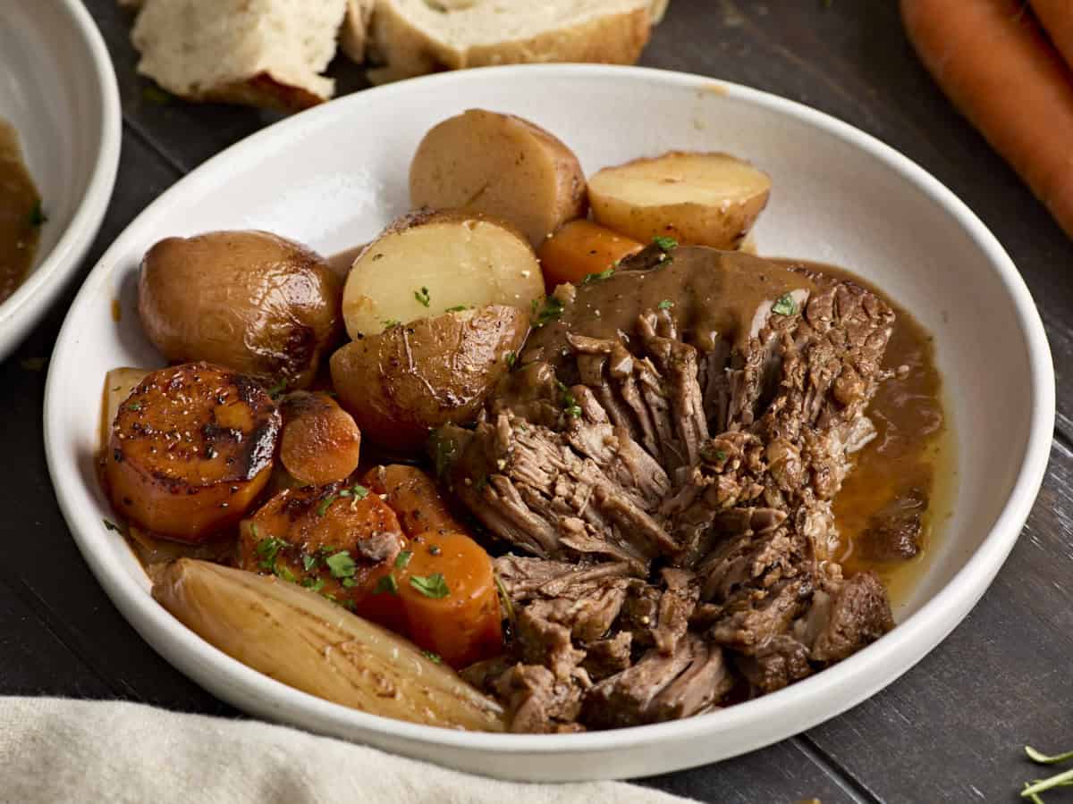 Side view of a pot roast and vegetables on a plate.