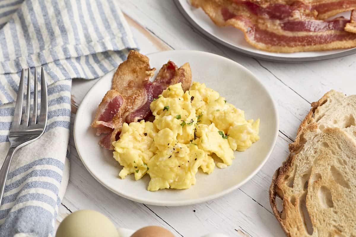 Side view of scrambled eggs with bacon on a plate.