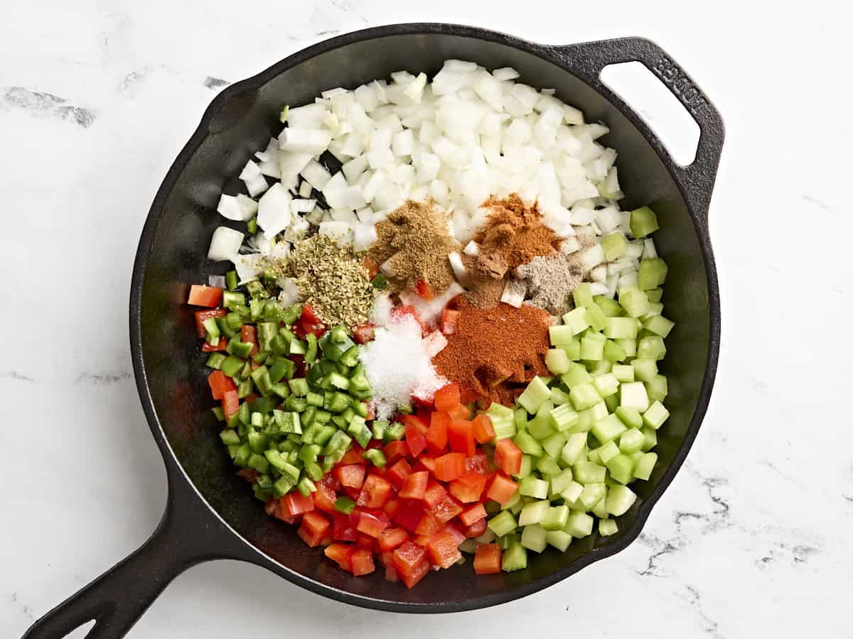 Mirepoix and seasonings added to a skillet to make shakshuka.