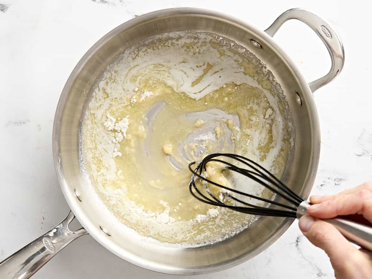 Butter and flour being whisked together in a saucepan to make a roux.