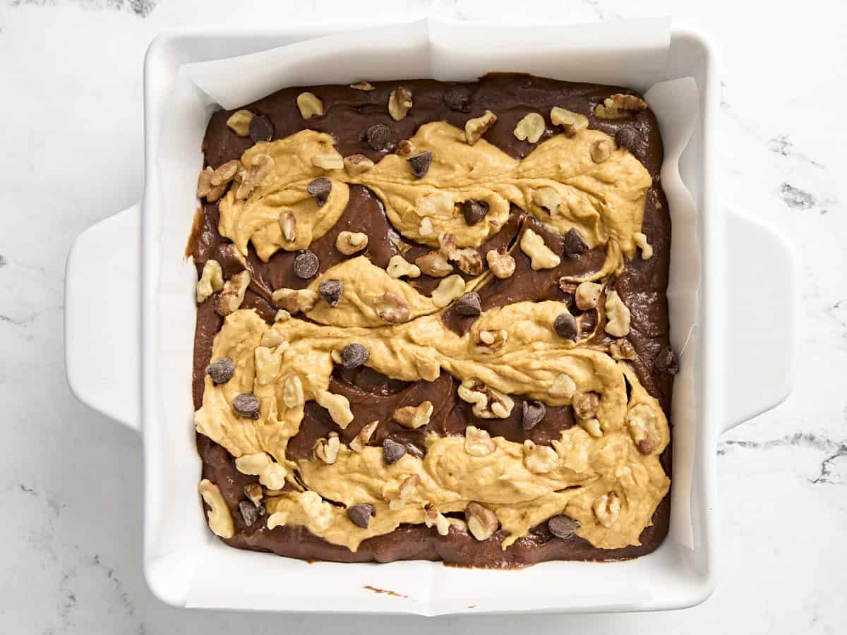 Pumpkin brownie batter topped with pecans and chocolate chips in a baking dish.