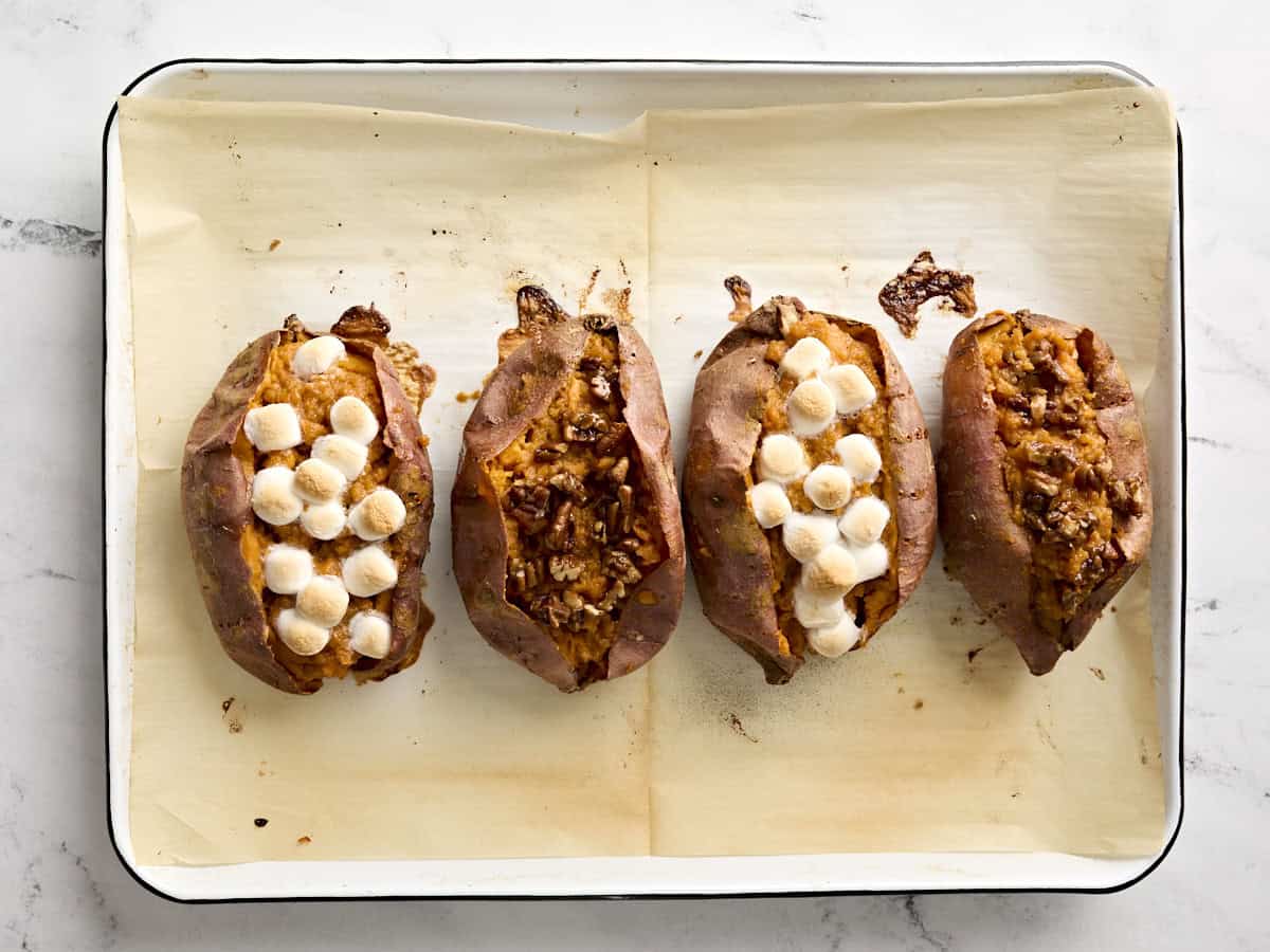 Stuffed twice baked sweet potatoes topped with marshmallows and candied pecans on a baking sheet.