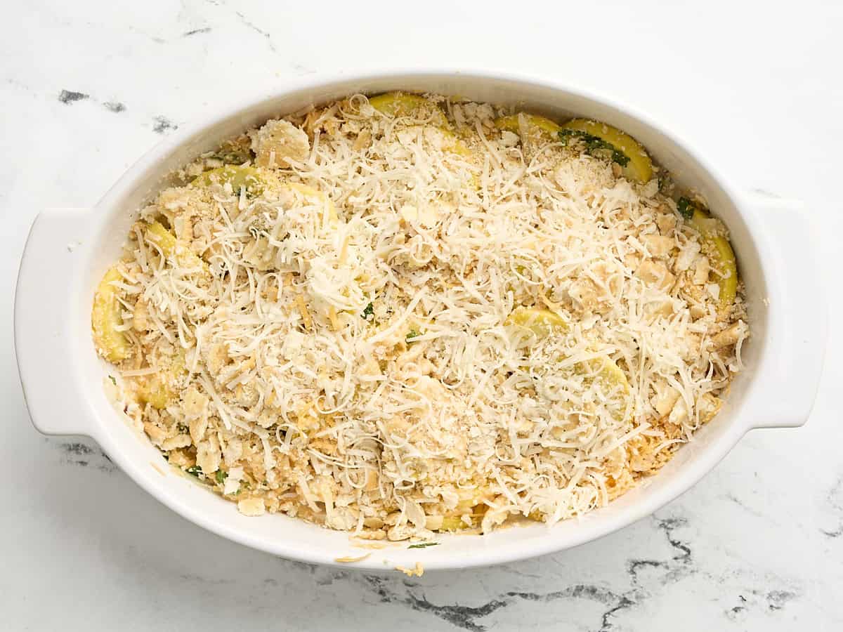 Squash casserole topped with shredded cheese in a casserole dish.