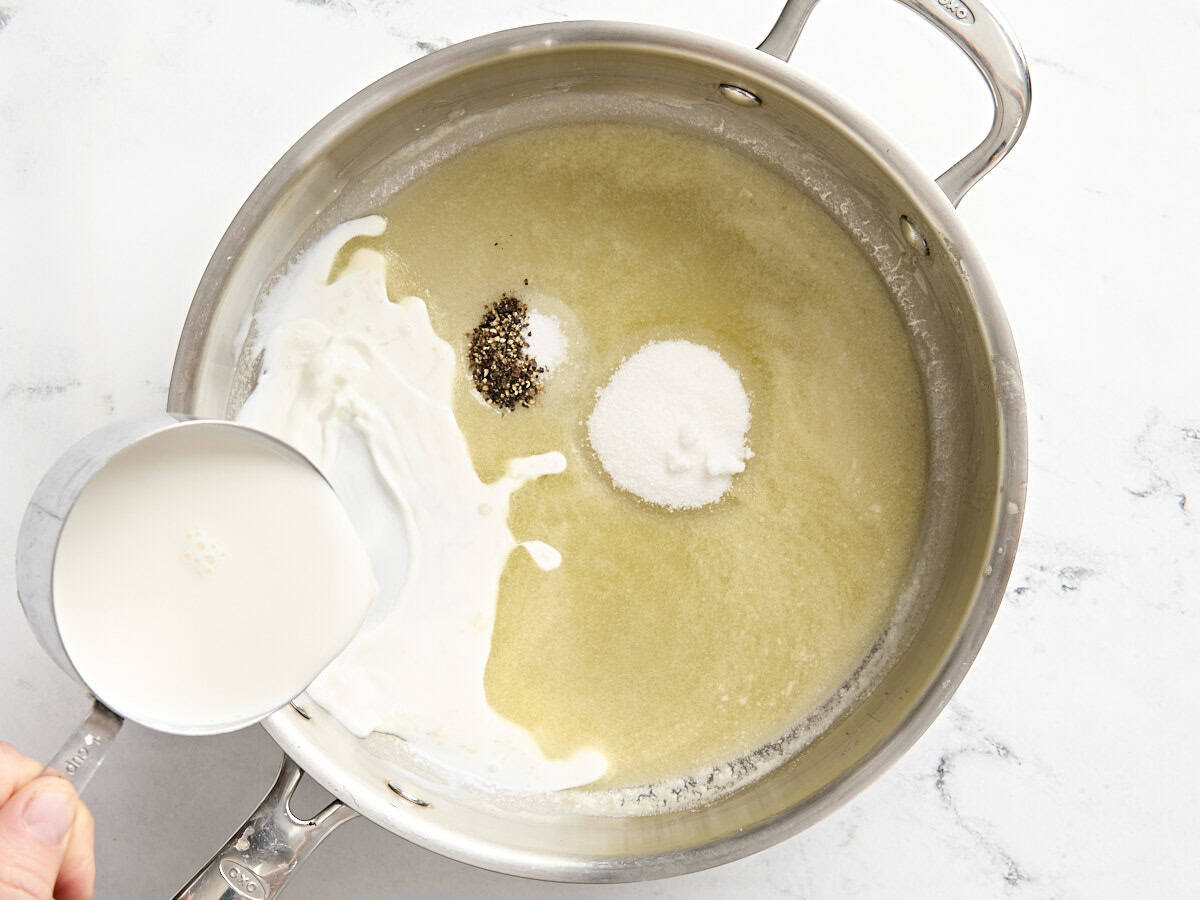 Milk, salt, and pepper added to a roux in a saucepan.