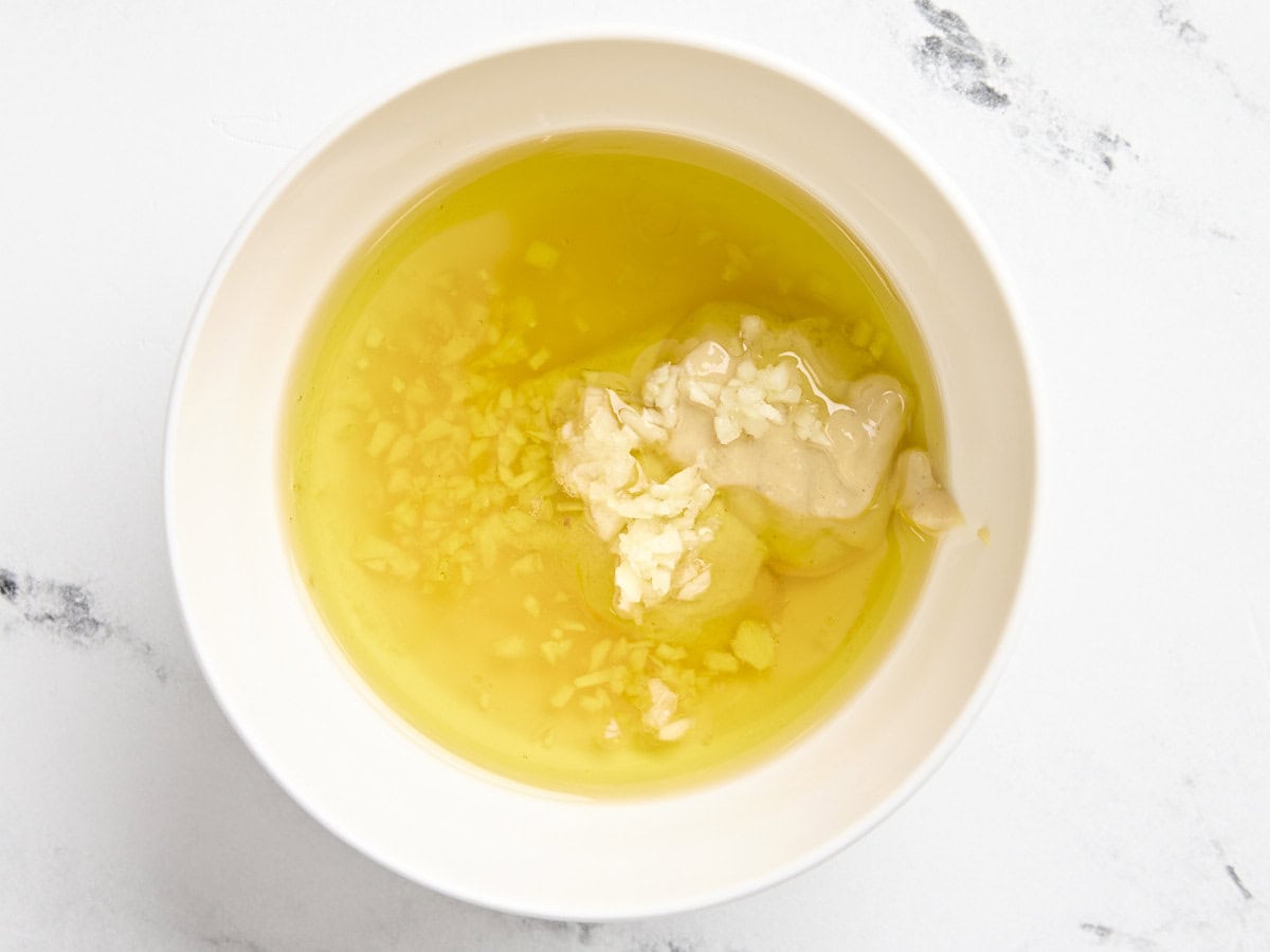 Olive oil, honey, garlic, and mustard in a mixing bowl to make a dressing for shaved Brussels sprouts salad.