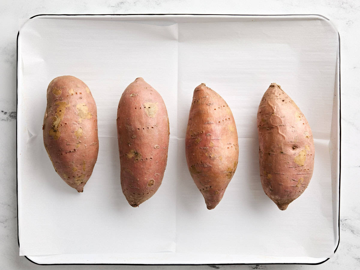 Baking sweet potatoes on a parchment lined baking sheet.