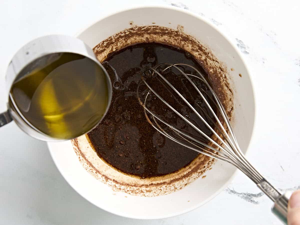 Spiced vinaigrette being whisked in a bowl with olive oil being poured in.