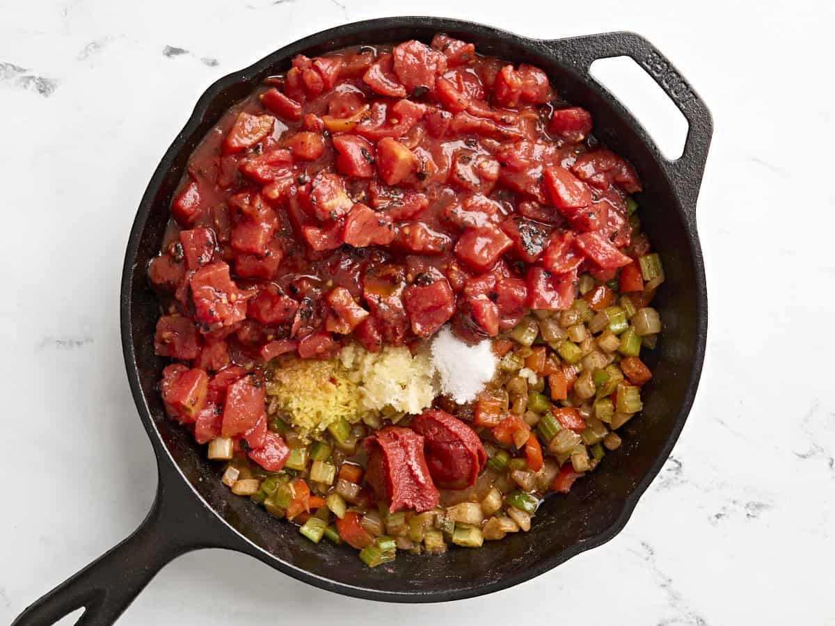 Diced tomatoes, garlic, and lemon juice added to softened vegetable in a skillet for shakshuka.