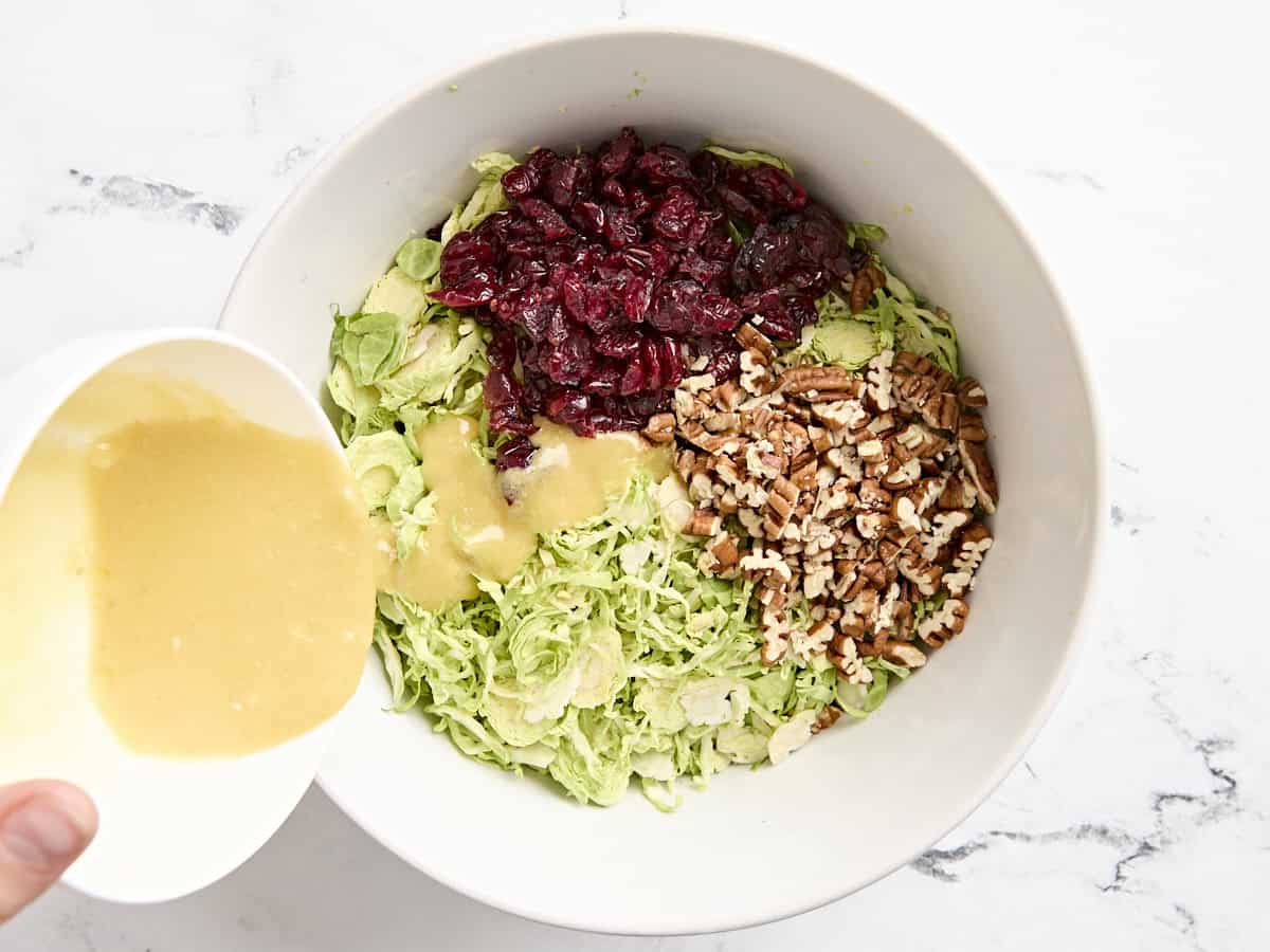 Pecans, craisins, and dressing added to a bowl with shaved brussels sprouts.