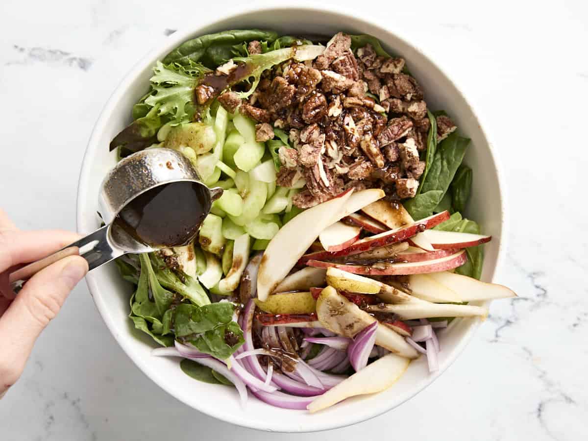 Pear, celery, and pecans salad in a bowl with dressing being poured on top.