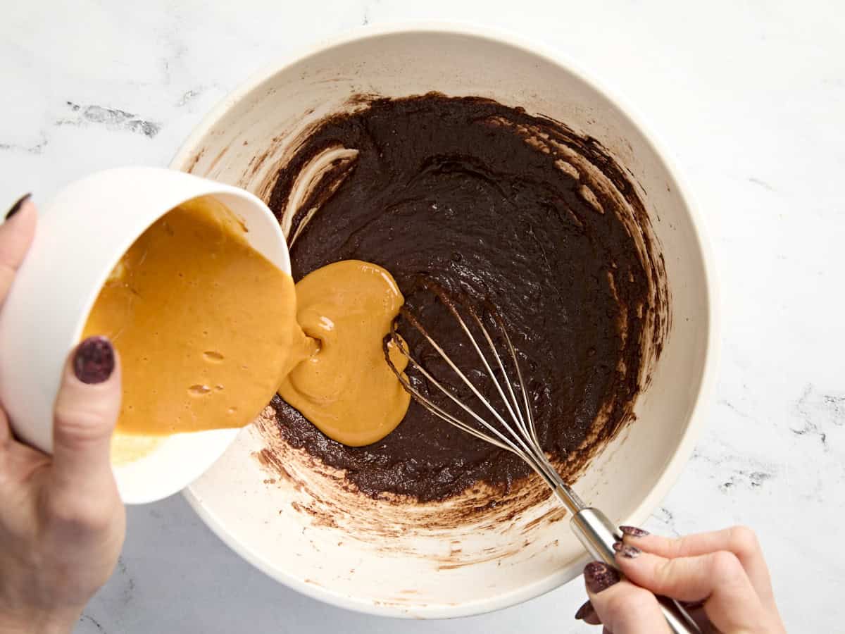 Pumpkin puree and egg mixture being poured into brownie batter in a baking dish.