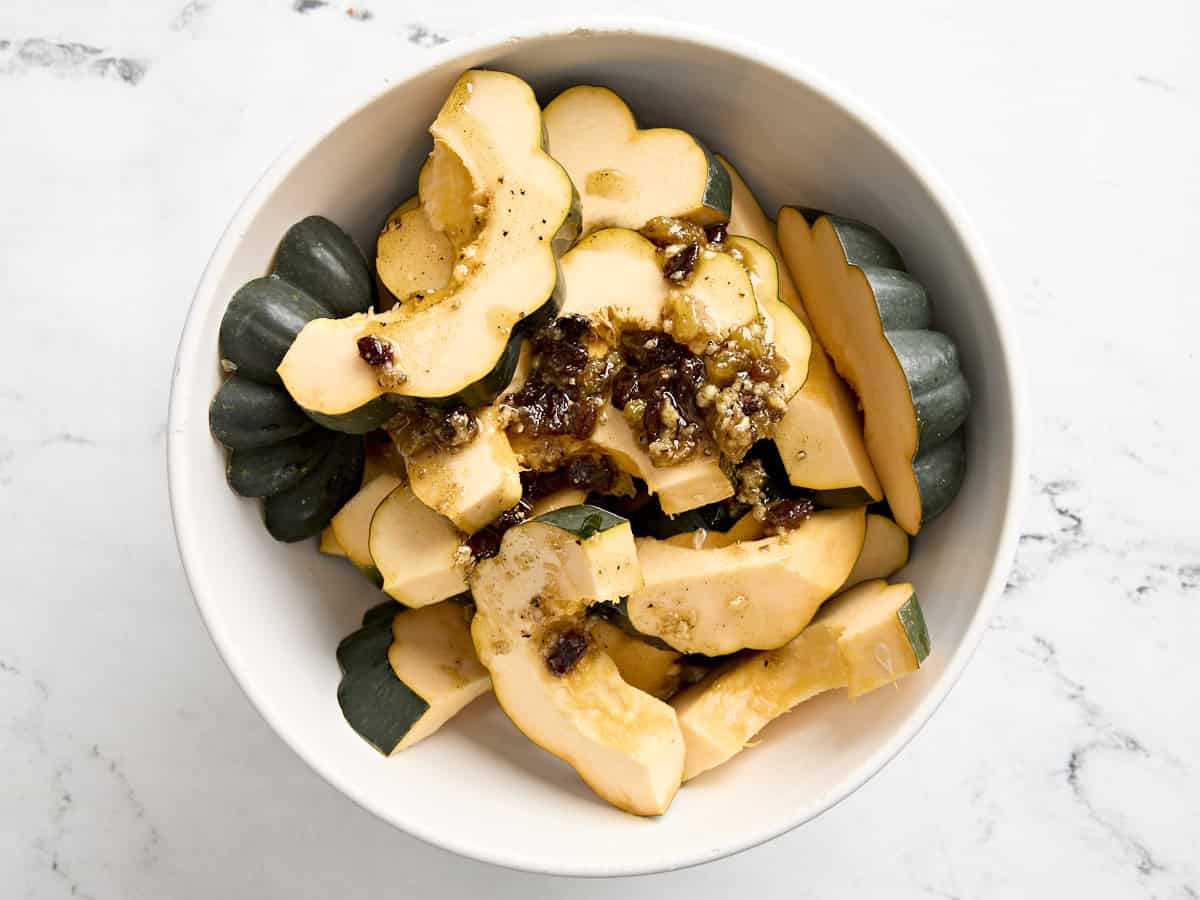 Oil and raisin marinade on acorn squash slices in a mixing bowl.