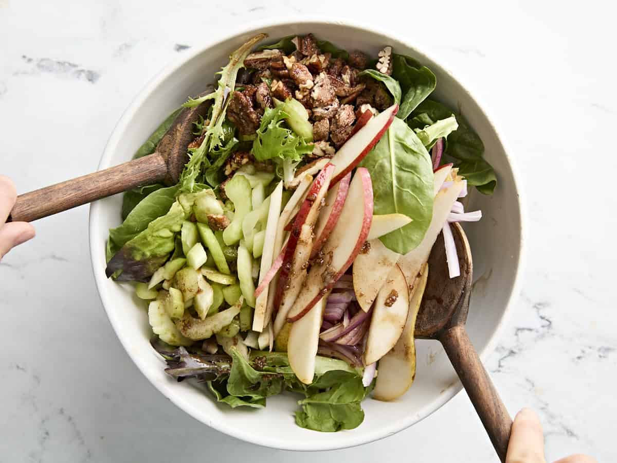 Pear, celery and pecan salad being tossed in a bowl.