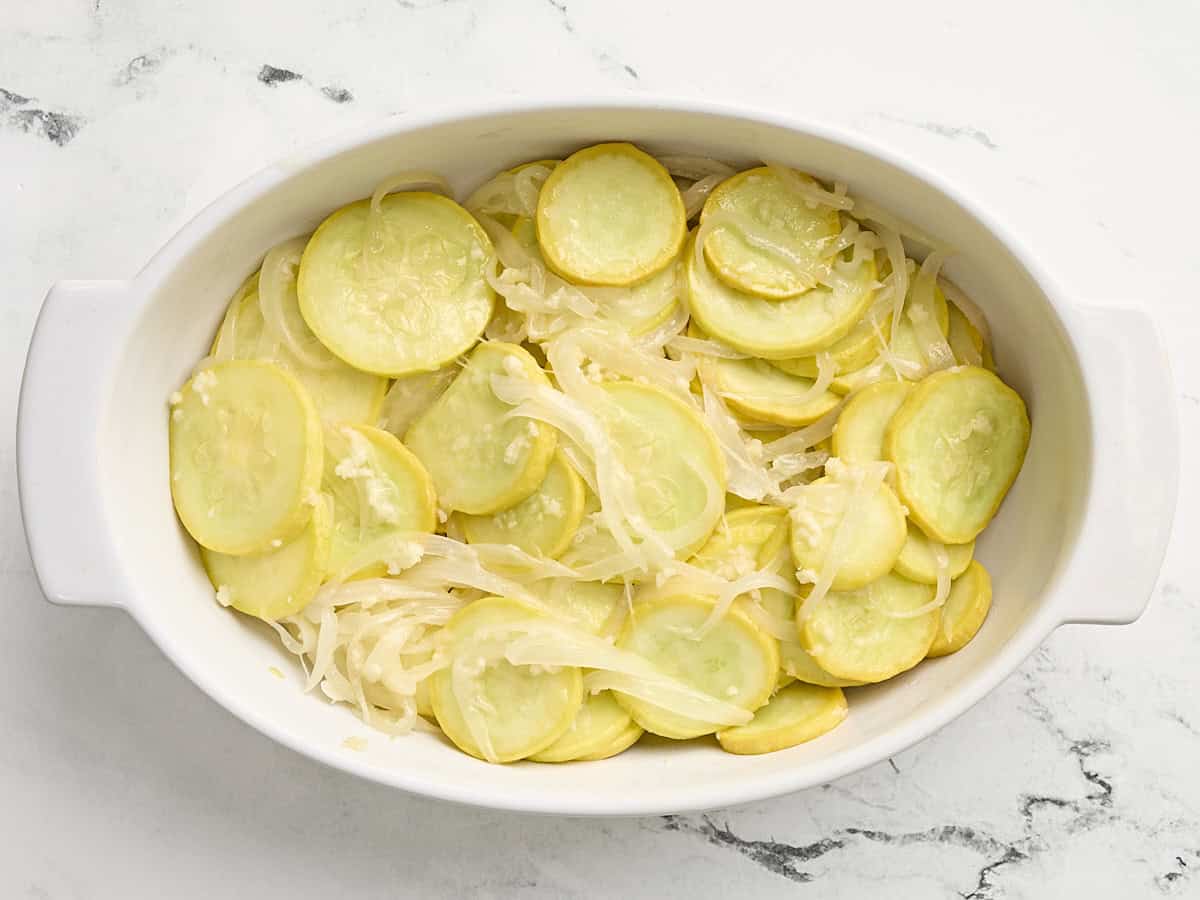 Slices of squash and onions in a casserole dish.