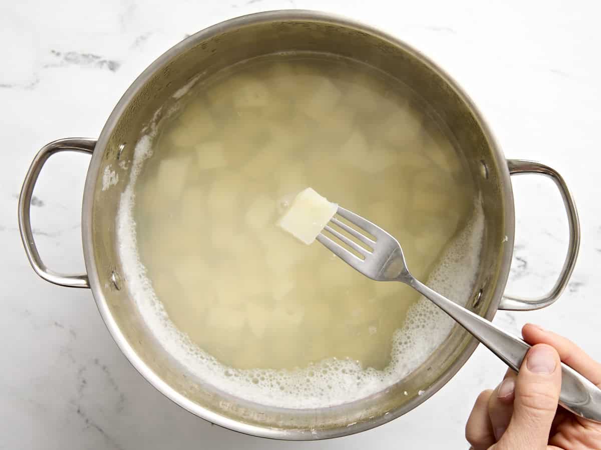 Diced potatoes in a saucepan of water with a fork checking for doneness.