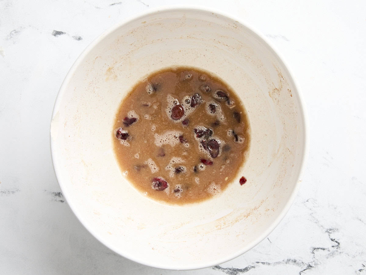 Dried cranberries soaking in a spiced lemon juice mixture in a mixing bowll.