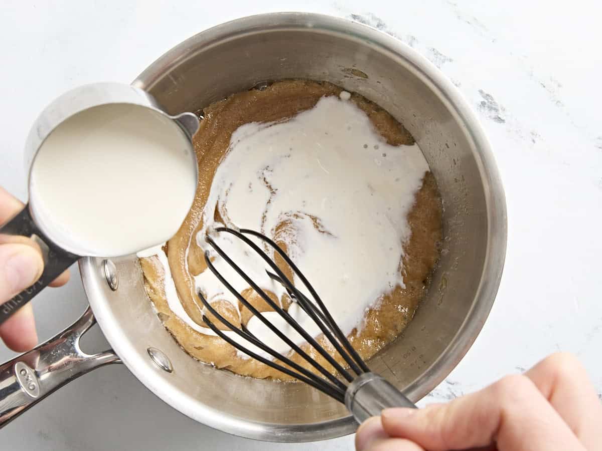 Heavy cream being whisked into melted butter and brown sugar to make caramel sauce.