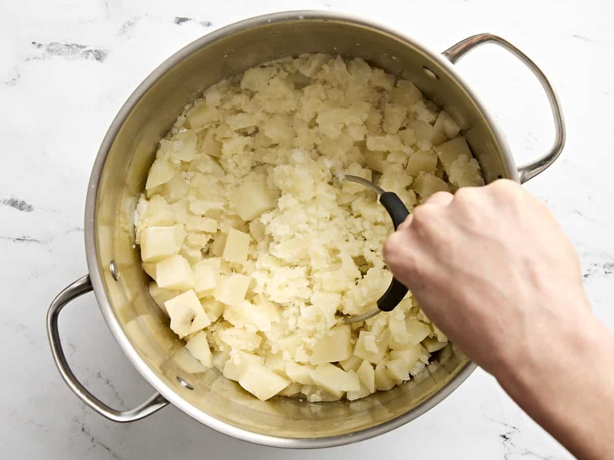 A hand mashing potatoes with a potato masher.