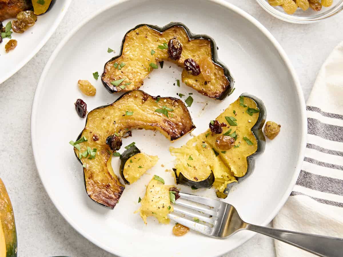 Overhead view of a roasted acorn squash pieces on a white plate with a fork digging into a slice.