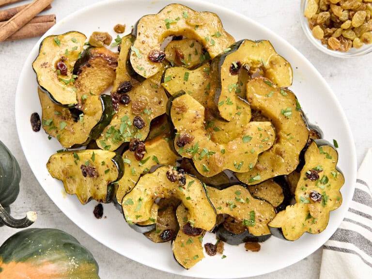 Roasted acorn squash with raisins and fresh parsley on a white serving platter.