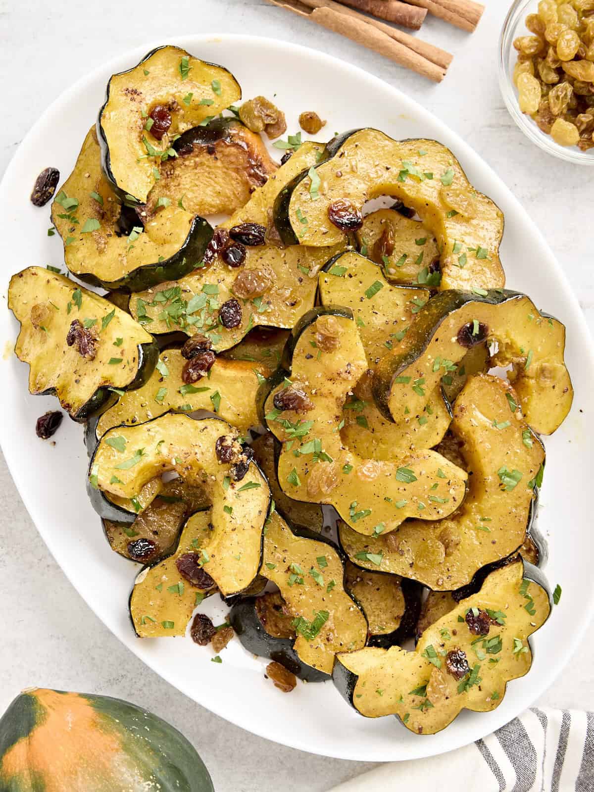 Roasted acorn squash with raisins and fresh parsley on a white serving platter.