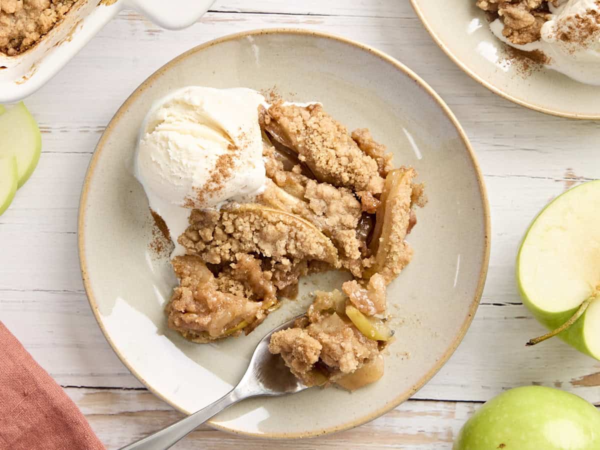 Overhead view of apple crumble and a scoop of vanilla ice cream on a plate with a fork taking some.