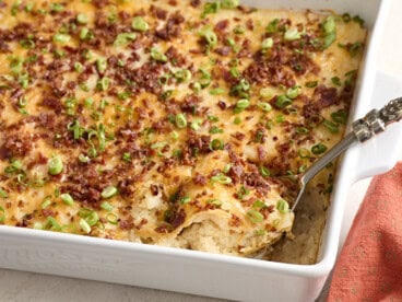 Side view of a spoon taking mashed potato casserole from a baking dish.