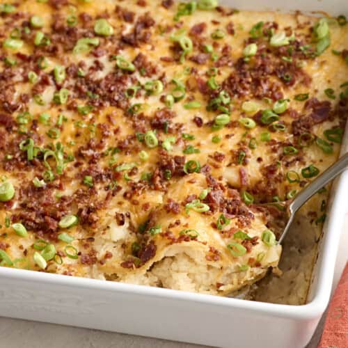 Side view of a spoon taking mashed potato casserole from a baking dish.