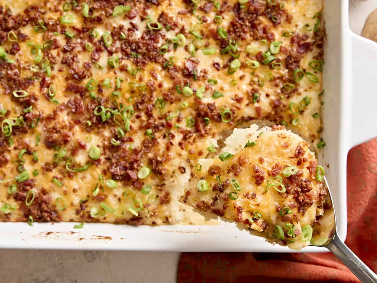 Overhead view of a spoon taking mashed potato casserole from a baking dish.