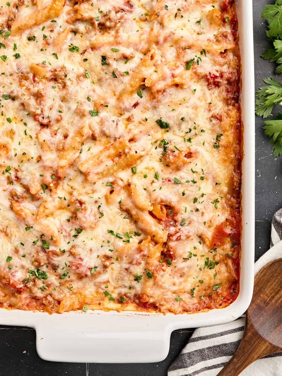 Overhead view of baked mostaccioli with a wooden serving spoon on the side.