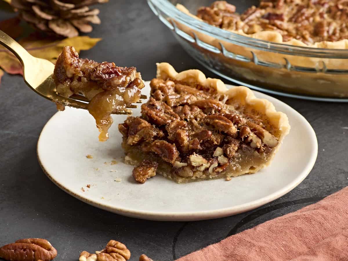 Side view of a slice of pecan pie on a white plate with a fork taking some.