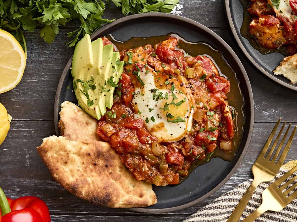 Overhead view of shakshuka on a plate with avocado and pitta bread.