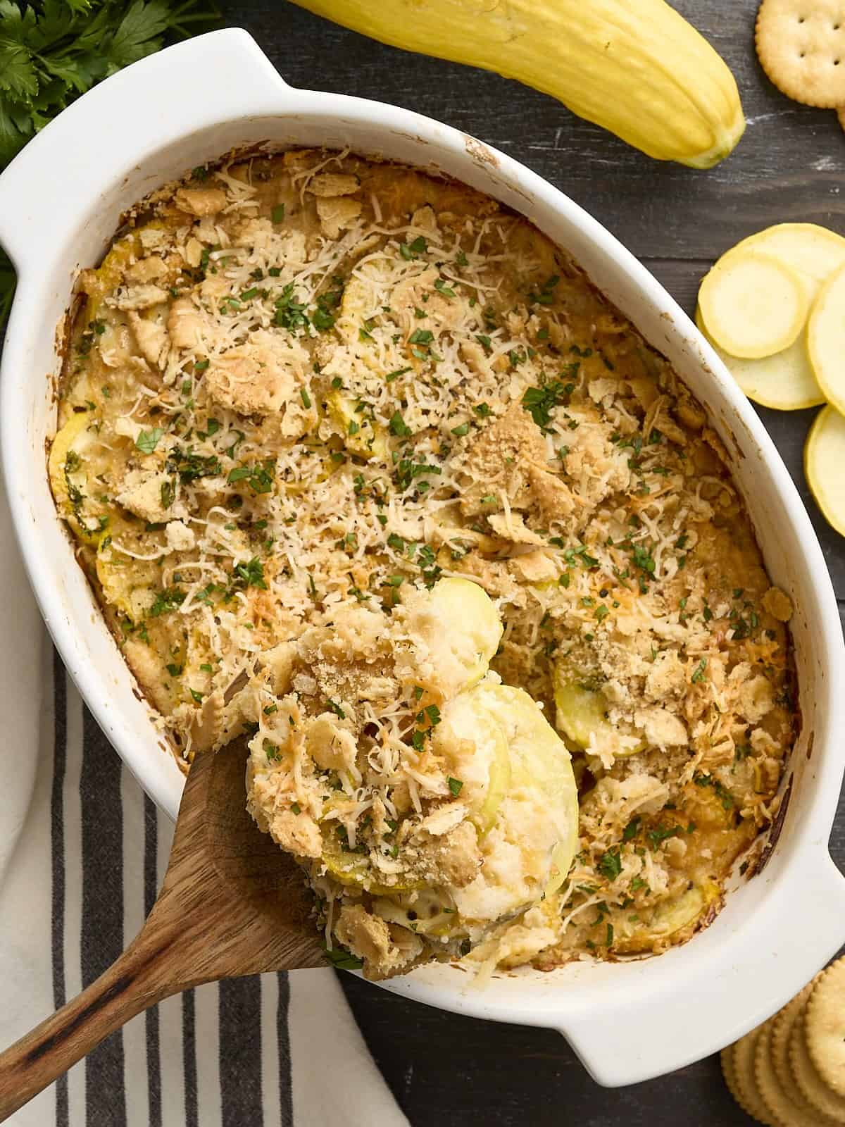 A wooden spoon scooping some squash casserole out of a casserole dish.