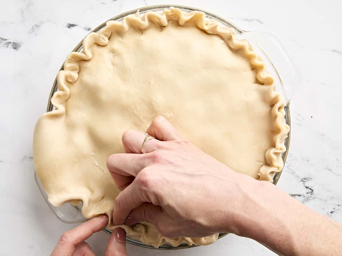 A hand crimping the edges of a turkey pot pie crust.