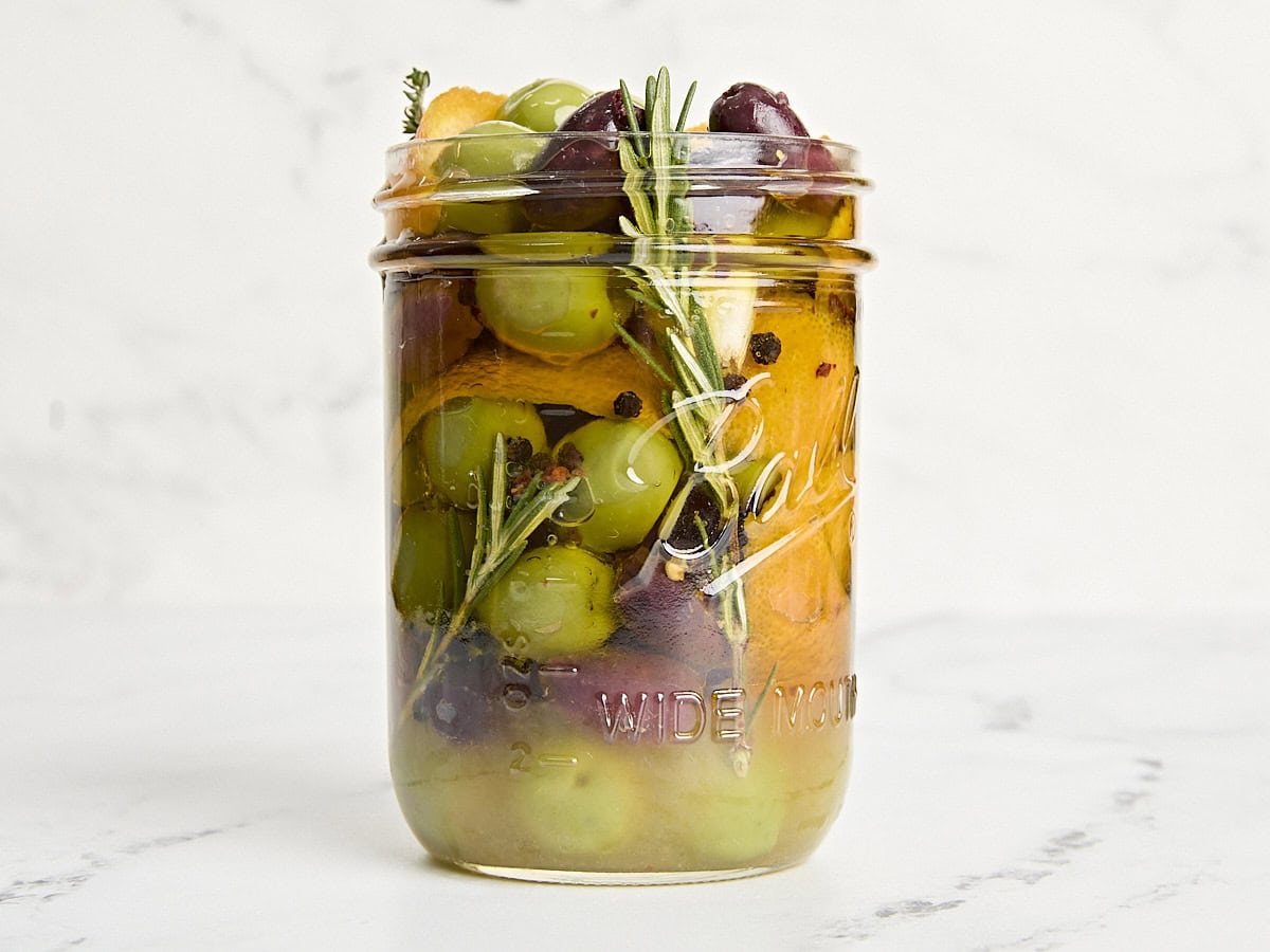 Side view of marinated olives in a mason jar.