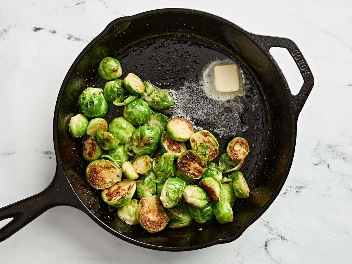 Butter added to sauteed brussels sprouts in a cast iron skillet.