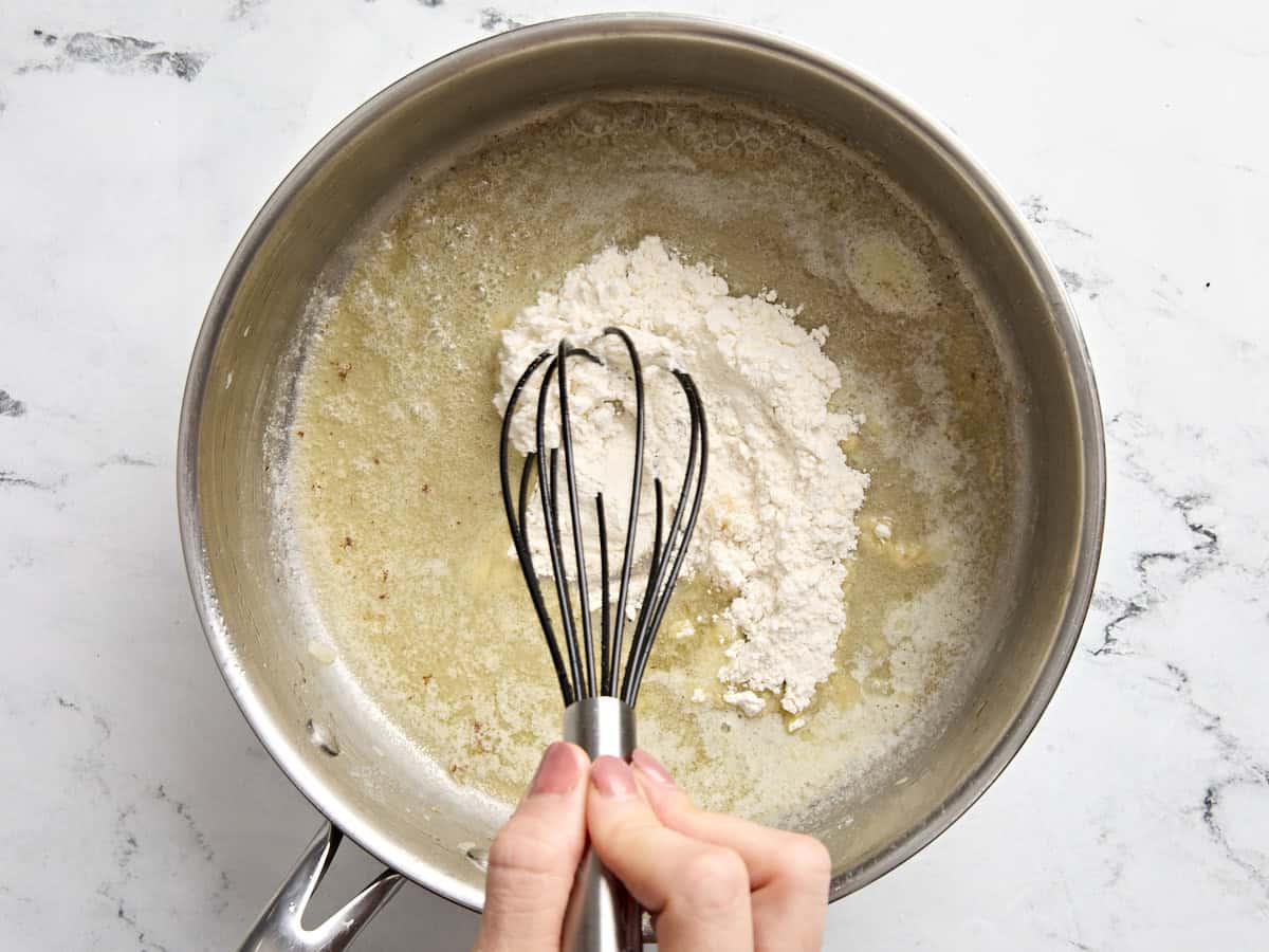 A hand whisking flour into melted butter in a saucepan.