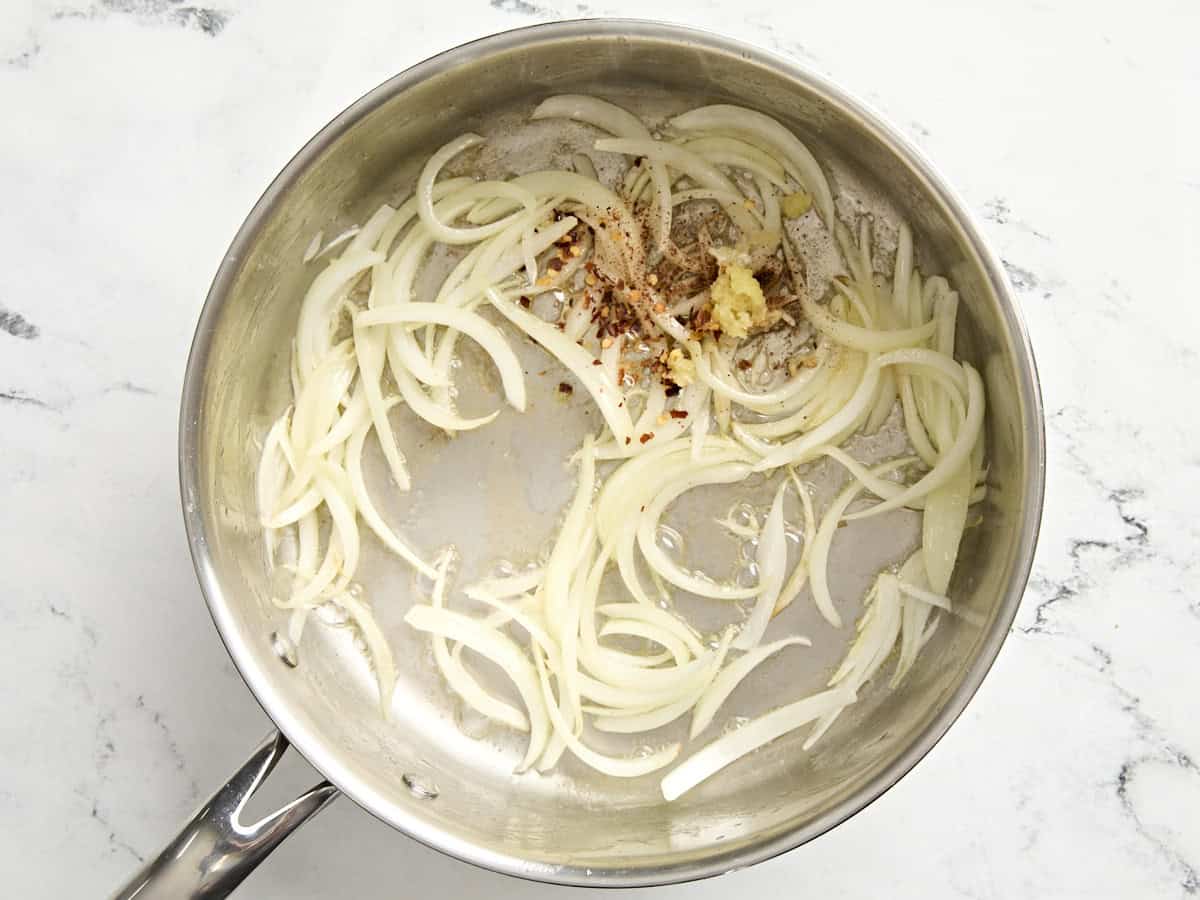 Sauted sliced onions in a skillet with seasonings and garlic added.