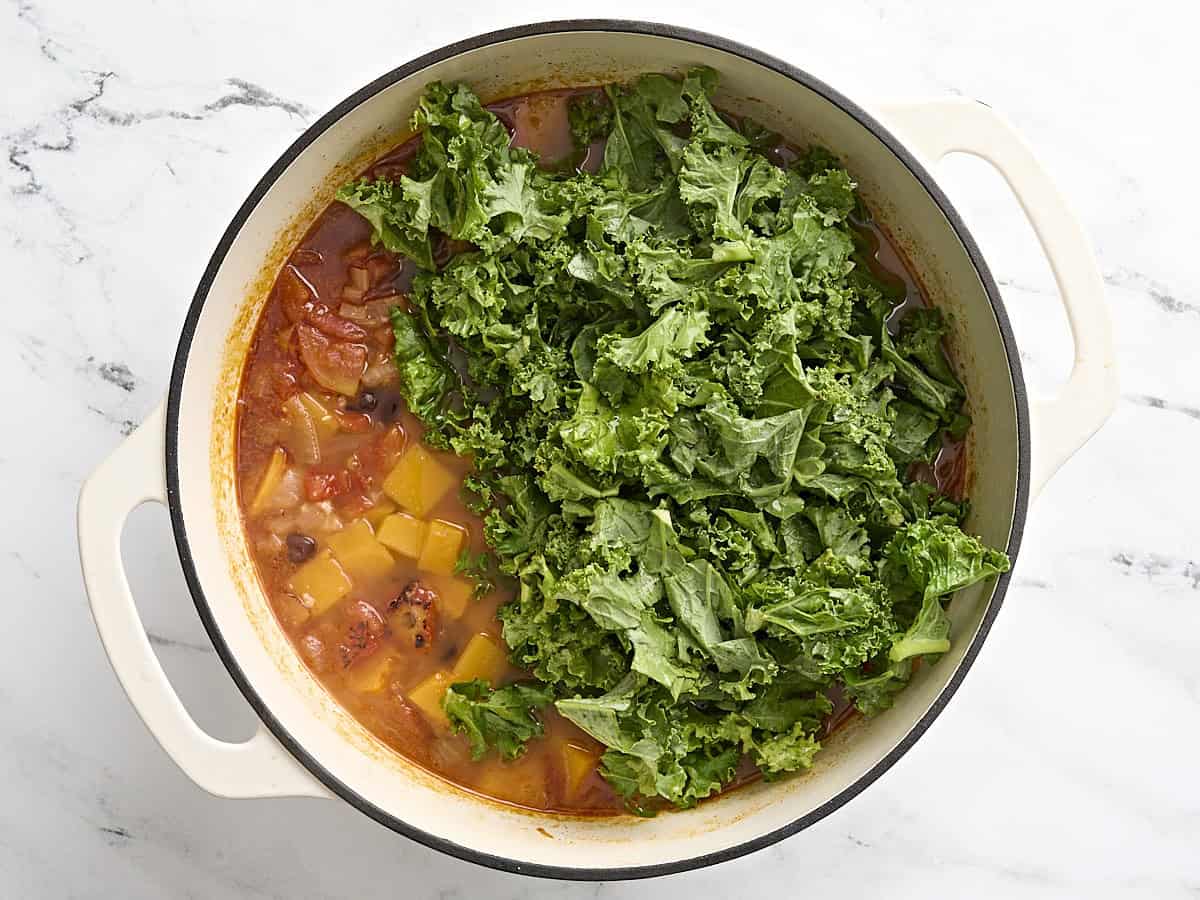 Chopped kale added to butternut squash and black bean soup in a dutch oven.