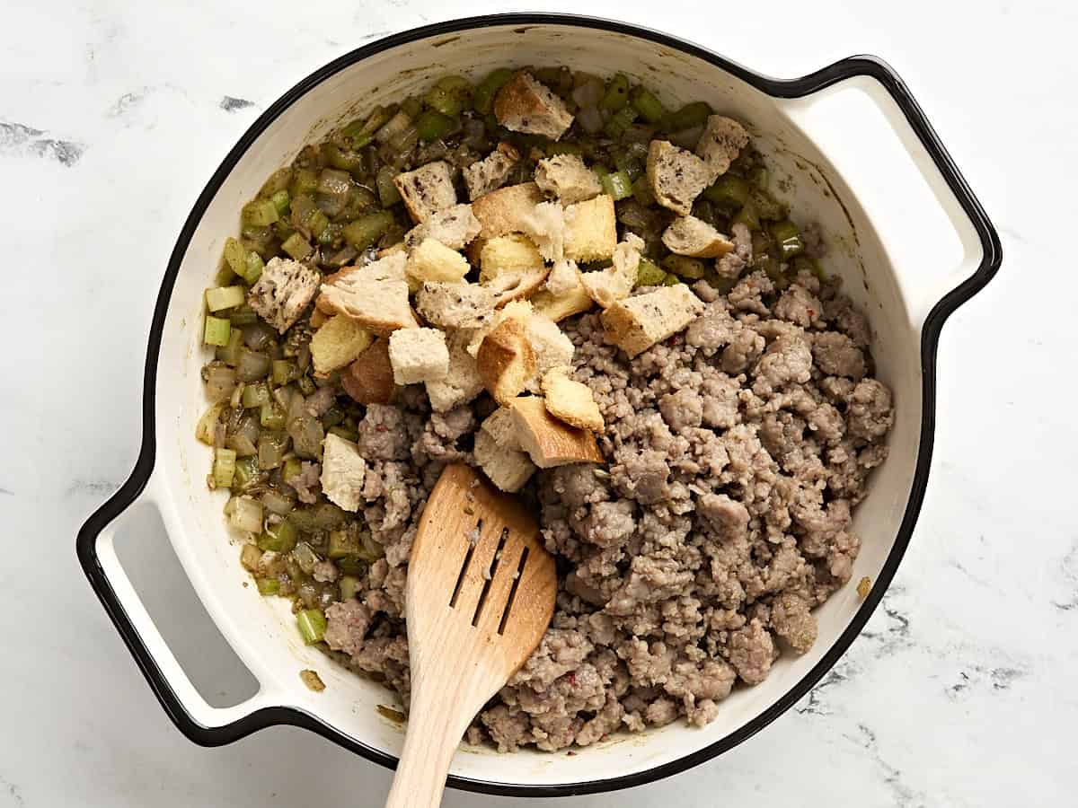 Toasted bread cubes and ground sausage added to cooked mirepoix in a skillet.