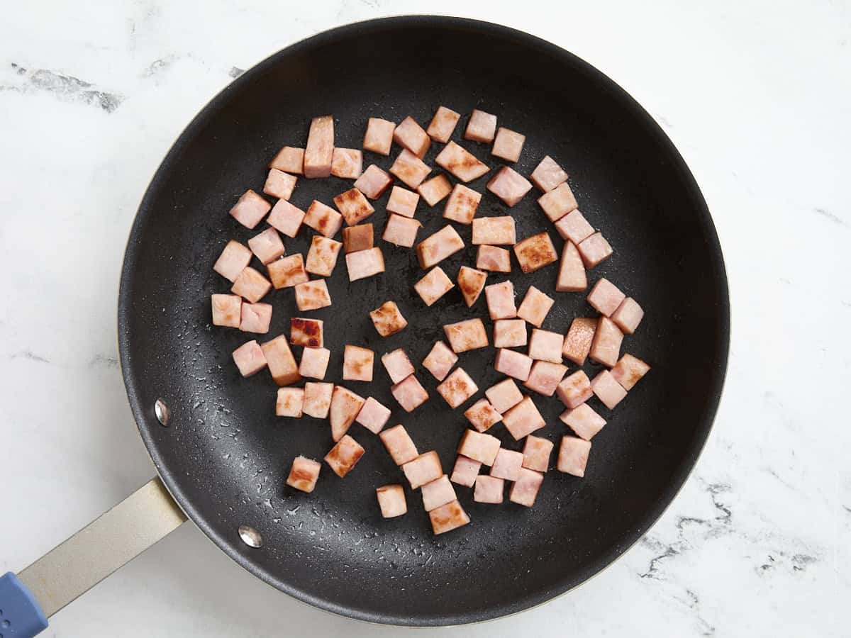 Diced ham steak frying in a skillet.