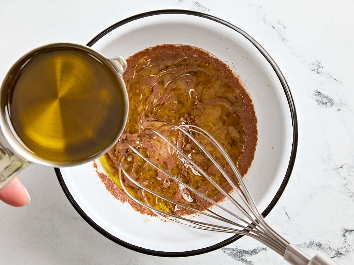 A whisk mixing ingredients for maple cinnamon vinaigrette in a bowl.