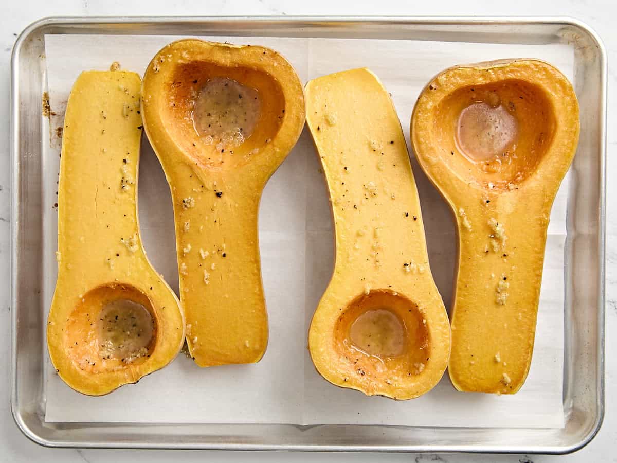 4 par baked butternut squash halves on a baking tray.